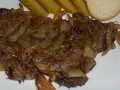 Kaszanka z cebulą, podana z ogórkami kiszonymi i kromką chleba. Danie wygląda apetycznie i sycąco.