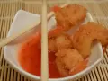 Chrupiące krewetki w panko zanurzone w słodko-kwaśnym sosie, gotowe do podania z pałeczkami.