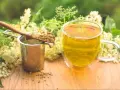 Aromaticzny napar z czarnego bzu, suszone kwiaty na łyżce i metalowe sitko.