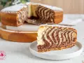 Stary przepis na ciasto zebra ujawnia swoje paski. Kawałek ciasta na talerzyku, a w tle całe ciasto posypane cukrem pudrem.