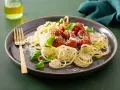 Pyszna keto kolacja: klopsiki w sosie pomidorowym na cukinii spaghetti, posypane parmezanem i listkami bazylii. Złoty widelec czeka.