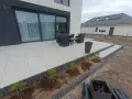 Nowy taras betonowy z meblami ogrodowymi i młodymi krzewami w przygotowanej rabacie.