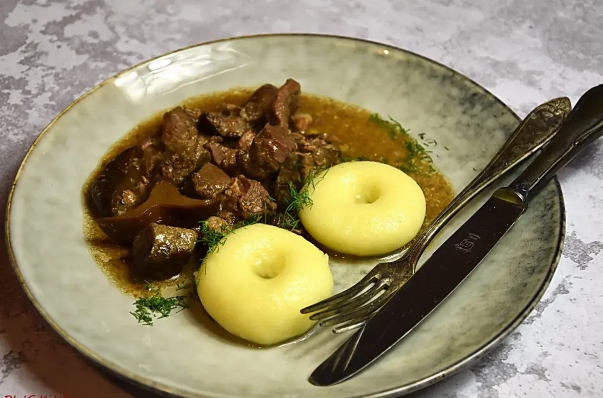 Gulasz z dzika z kluskami śląskimi, ozdobiony koperkiem. Aromatyczne danie, które rozpływa się w ustach.
