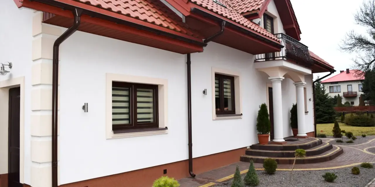 Elegancki cokół na elewacji domu, wykończony brązową, ziarnistą strukturą, chroni ściany przed wilgocią.