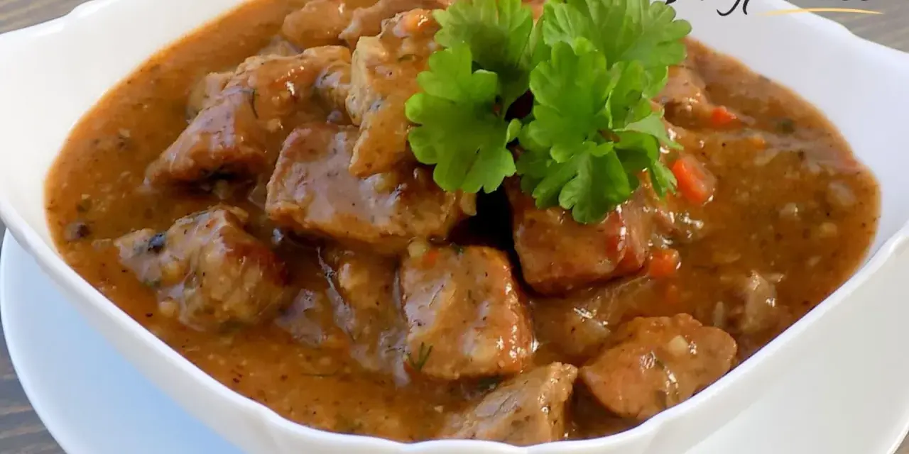 Aromaticzny gulasz z karkówki w sosie własnym, udekorowany gałązką natki pietruszki. Idealny na sycący obiad.