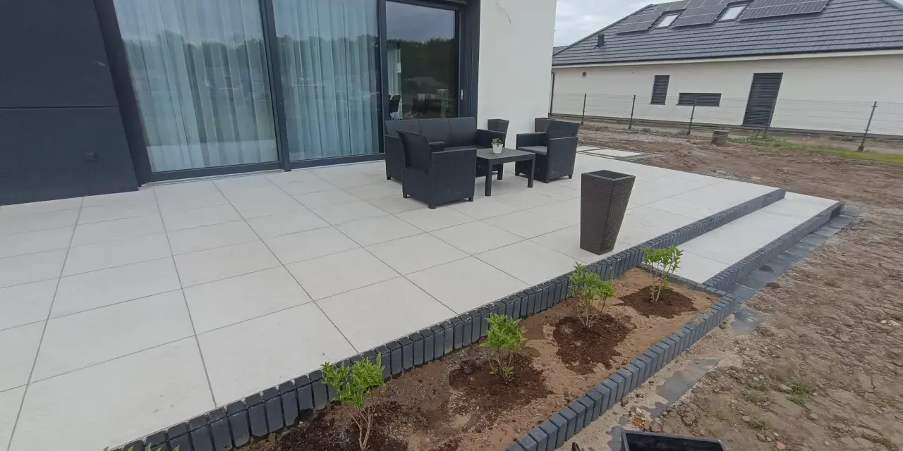 Nowy taras betonowy z meblami ogrodowymi i młodymi krzewami w przygotowanej rabacie.