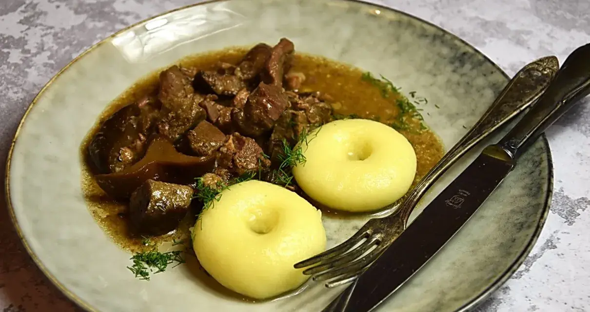 Gulasz z dzika z kluskami śląskimi, ozdobiony koperkiem. Aromatyczne danie, które rozpływa się w ustach.