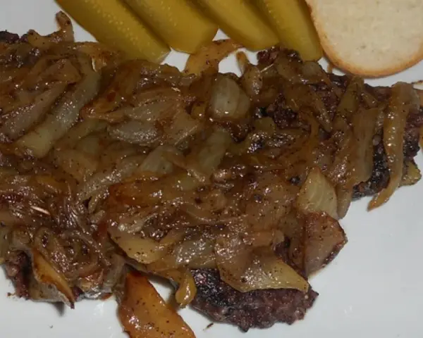 Kaszanka z cebulą, podana z ogórkami kiszonymi i kromką chleba. Danie wygląda apetycznie i sycąco.