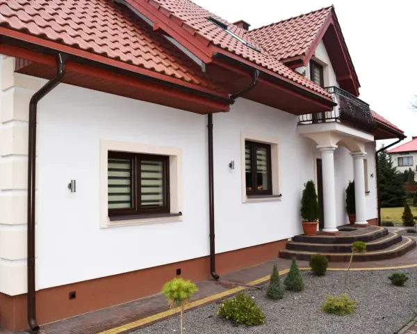 Elegancki cokół na elewacji domu, wykończony brązową, ziarnistą strukturą, chroni ściany przed wilgocią.