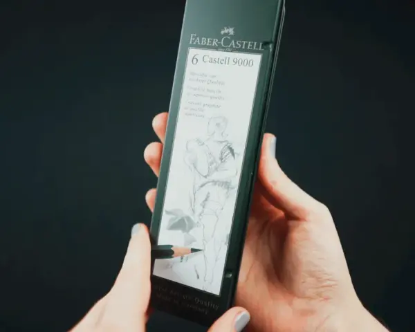 Dłonie trzymają opakowanie z sześcioma ołówkami Faber-Castell 9000. Jeden ołówek rysuje szkic postaci.