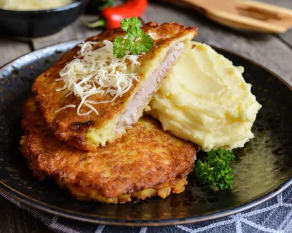 Złocisty kotlet po parysku, nadziany szynką i serem, podany z purée ziemniaczanym i natką pietruszki. Pyszne danie na obiad.