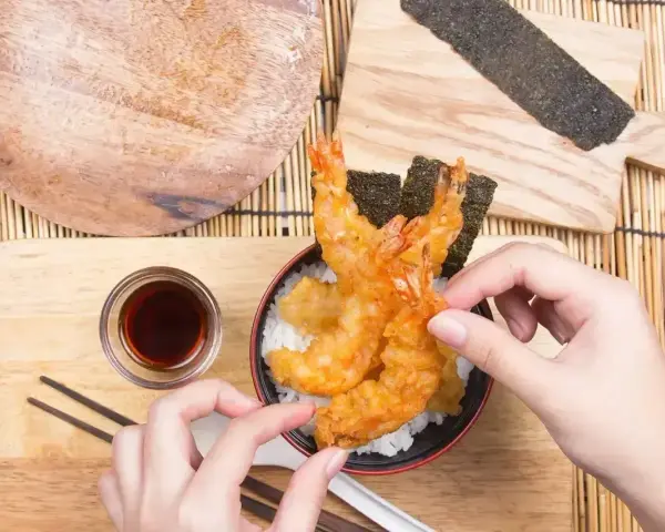 Ręce układają chrupiące krewetki tempura na ryżu. Idealny przepis na tempurę do domowego obiadu.