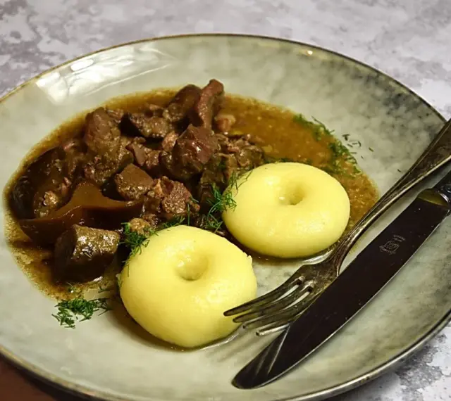 Gulasz z dzika z kluskami śląskimi, ozdobiony koperkiem. Aromatyczne danie, które rozpływa się w ustach.