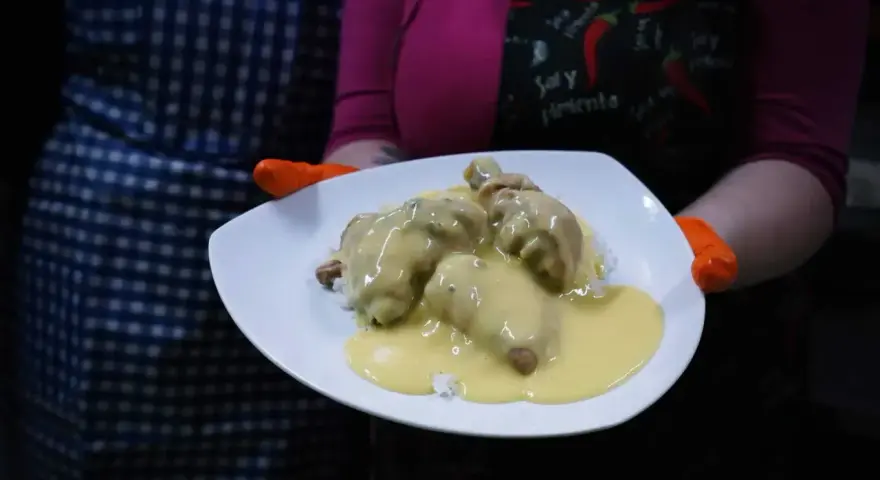 Porcja potrawki z kurczaka w kremowym sosie, podana na ryżu. Danie prezentowane na białym talerzu, trzymanym przez osobę w pomarańczowych rękawiczkach.