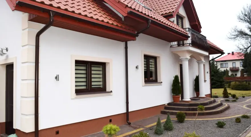 Elegancki cokół na elewacji domu, wykończony brązową, ziarnistą strukturą, chroni ściany przed wilgocią.
