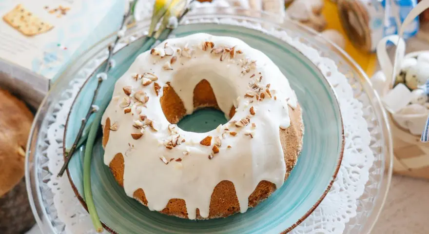 Babka piaskowa przepis babci, udekorowana lukrem i orzechami, na talerzu z wiosennymi akcentami.