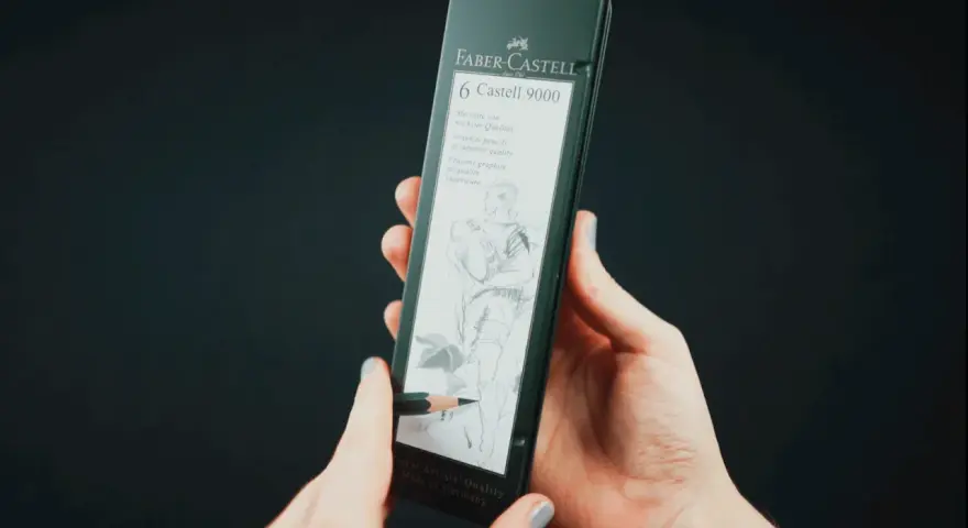 Dłonie trzymają opakowanie z sześcioma ołówkami Faber-Castell 9000. Jeden ołówek rysuje szkic postaci.
