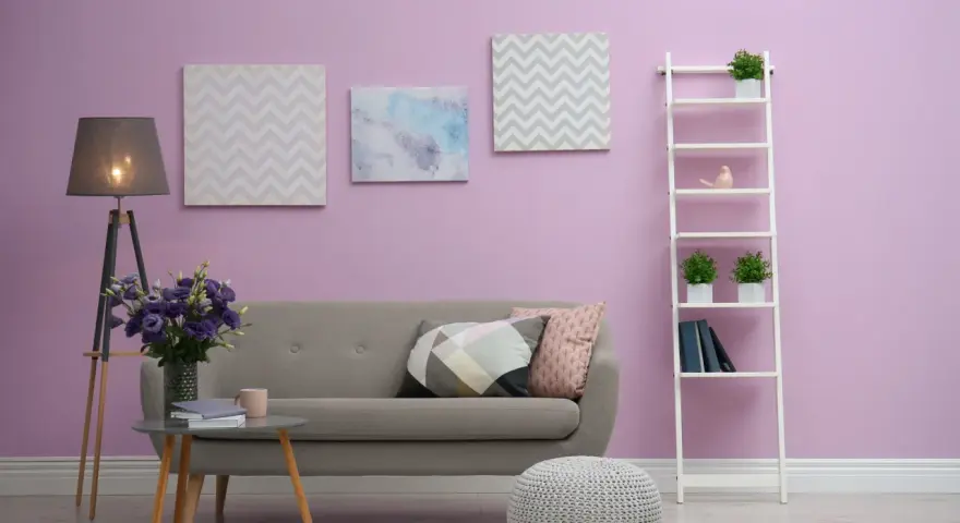 Przytulny salon z szarą kanapą, stolikiem kawowym z bukietem fioletowych kwiatów i dekoracjami na ścianie w kolorze liliowym.
