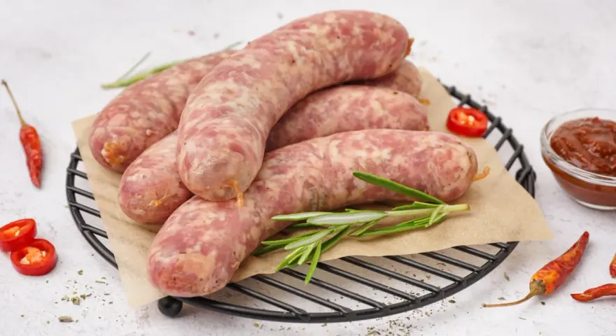 Surowa biała kiełbasa na ruszcie z rozmarynem, papryczkami chili i sosem. Dowiedz się, ile gotować białą kiełbasę, by była idealna.