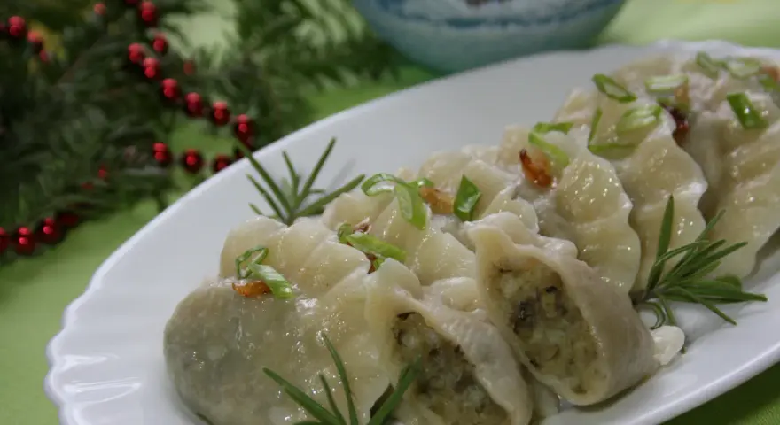 Pyszne pierogi ukraińskie, udekorowane szczypiorkiem i rozmarynem, prezentują się apetycznie na białym talerzu.