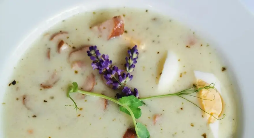 Aromaticzny żurek z kiełbasą i jajkiem, ozdobiony gałązką lawendy i kiełkami.