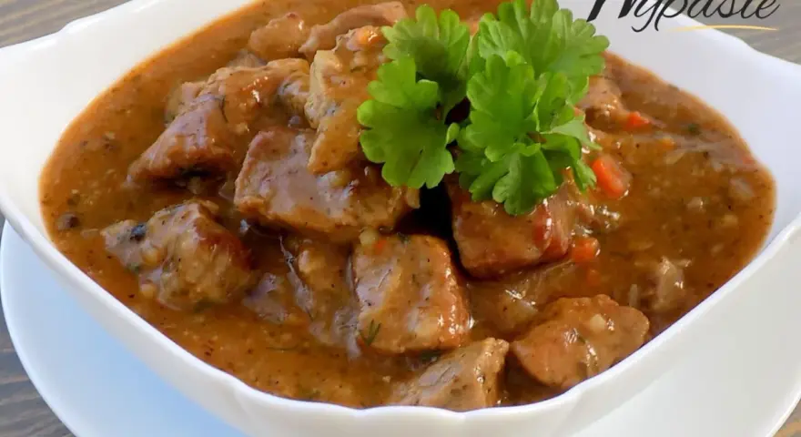 Aromaticzny gulasz z karkówki w sosie własnym, udekorowany gałązką natki pietruszki. Idealny na sycący obiad.