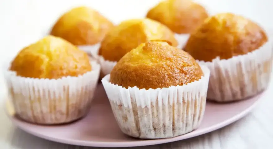 Idealny przepis na wilgotne i puszyste muffinki. Złociste, pachnące babeczki na różowym talerzyku.