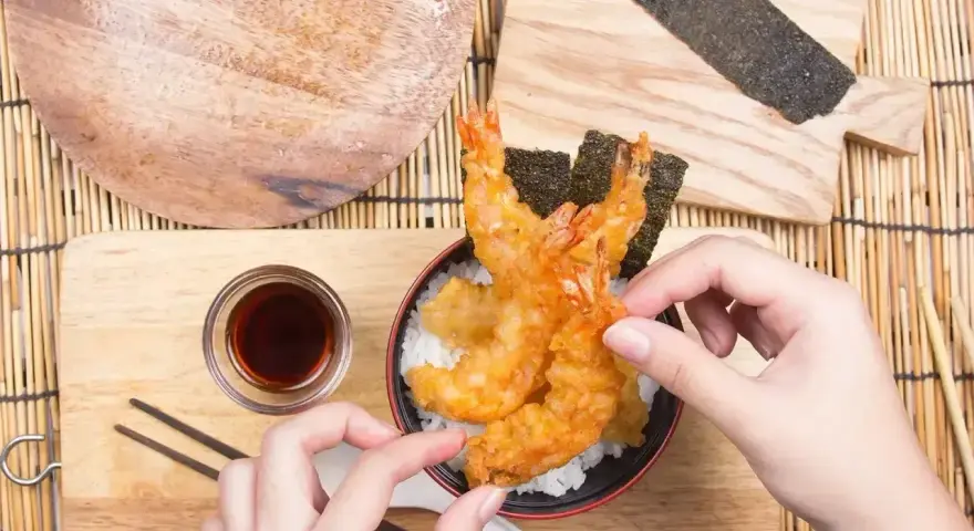 Ręce układają chrupiące krewetki tempura na ryżu. Idealny przepis na tempurę do domowego obiadu.