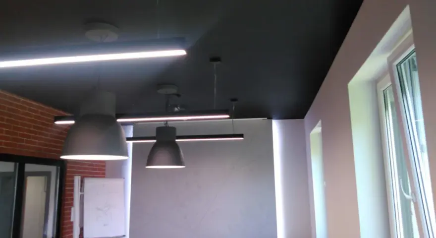Nowoczesne biuro z czarnym sufitem (RAL 9004), wiszącymi lampami i ceglaną ścianą.