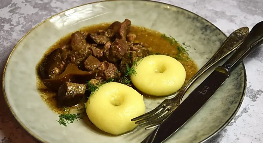Gulasz z dzika z kluskami śląskimi, ozdobiony koperkiem. Aromatyczne danie, które rozpływa się w ustach.