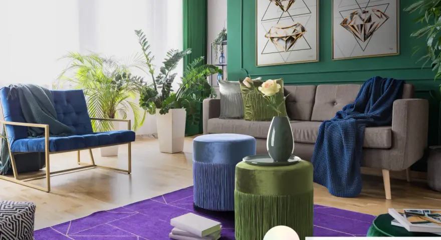 Elegancki salon z sofą, fotelem i pufami. Dominują głębokie zielenie, granat i fiolet. Pufy w odcieniach niebieskiego i **kolor seledynowy** dodają uroku.