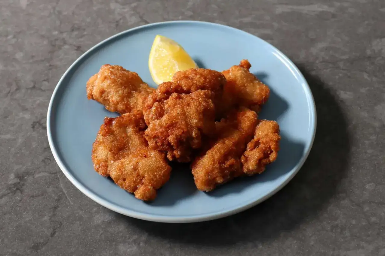 Chrupiące kawałki kurczaka karaage na niebieskim talerzu, ozdobione ćwiartką cytryny.