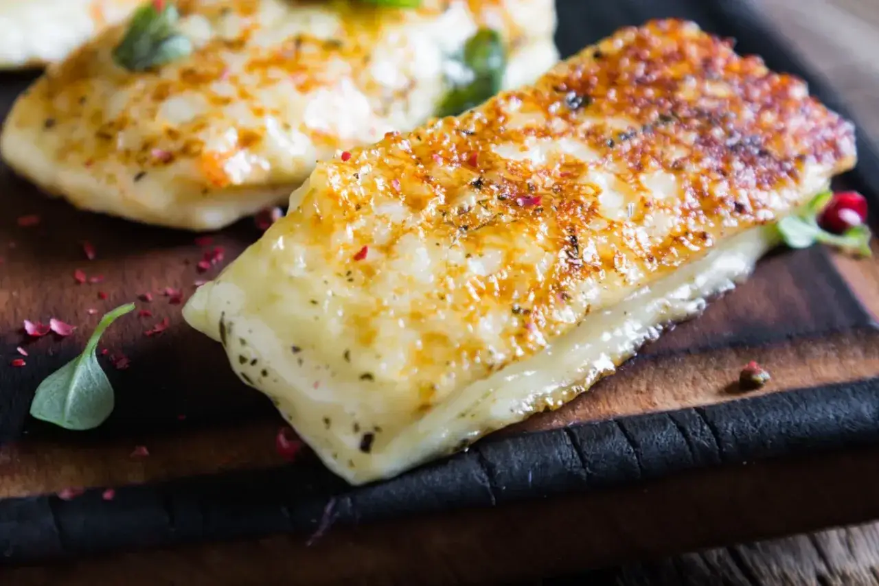 Złociste halloumi z grilla, lekko przypieczone, z ziołami i pieprzem, na drewnianej desce.