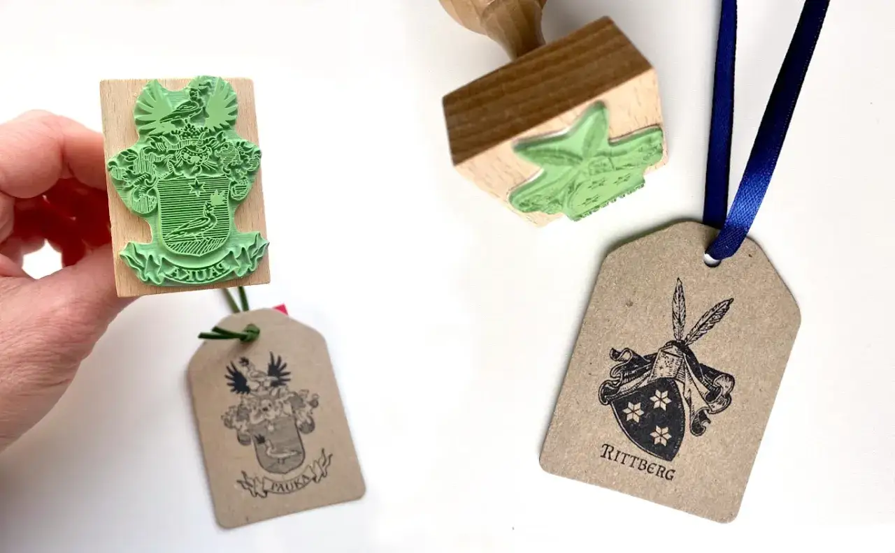 Drewniane stemple z herbami, idealne do tworzenia własnych exlibris. Jeden stempel z zieloną gumką, drugi z czarnym nadrukiem na brązowej etykiecie.