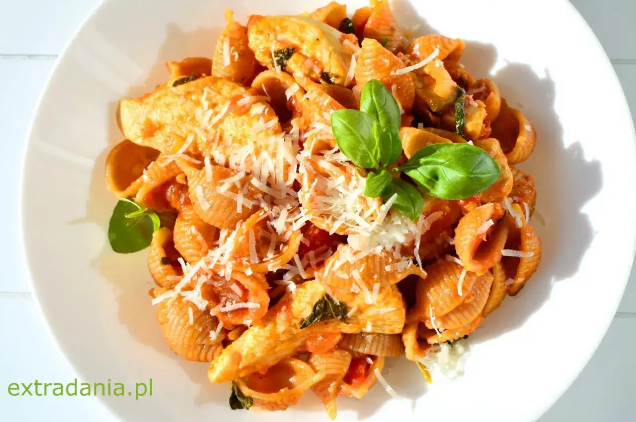 Pyszny makaron z kurczakiem w sosie pomidorowym, posypany parmezanem i udekorowany bazylią.