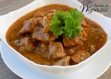 Aromaticzny gulasz z karkówki w sosie własnym, udekorowany gałązką natki pietruszki. Idealny na sycący obiad.