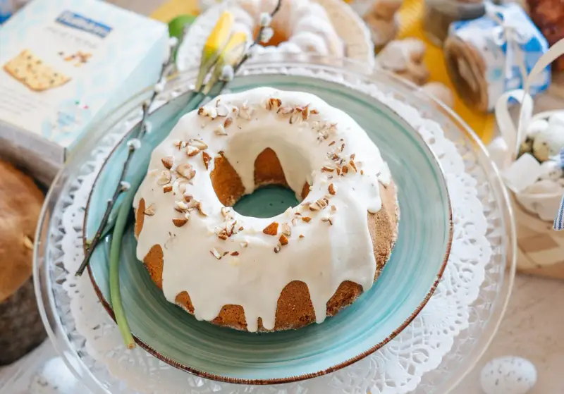 Babka piaskowa przepis babci, udekorowana lukrem i orzechami, na talerzu z wiosennymi akcentami.