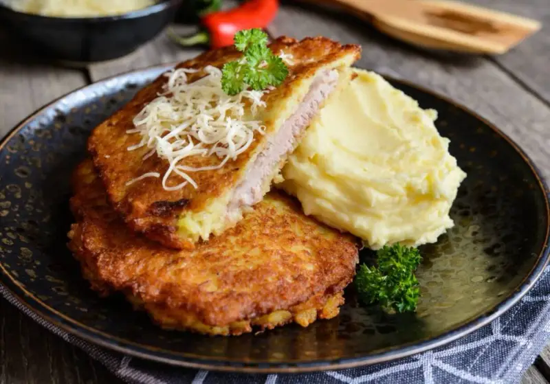 Złocisty kotlet po parysku, nadziany szynką i serem, podany z purée ziemniaczanym i natką pietruszki. Pyszne danie na obiad.